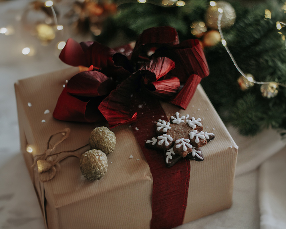 Kalėdų dovana suvyniota į popierių, perrišta lankeliu ir papuošta sausainiu.