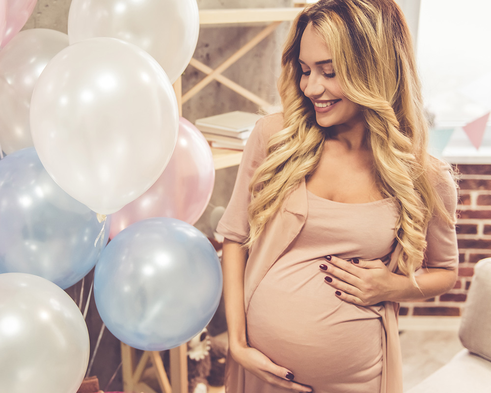 Nėščia moteris su šypsena žvelgia į spalvingus balionus kūdikio sutiktuvių vakarėlyje („baby shower“)