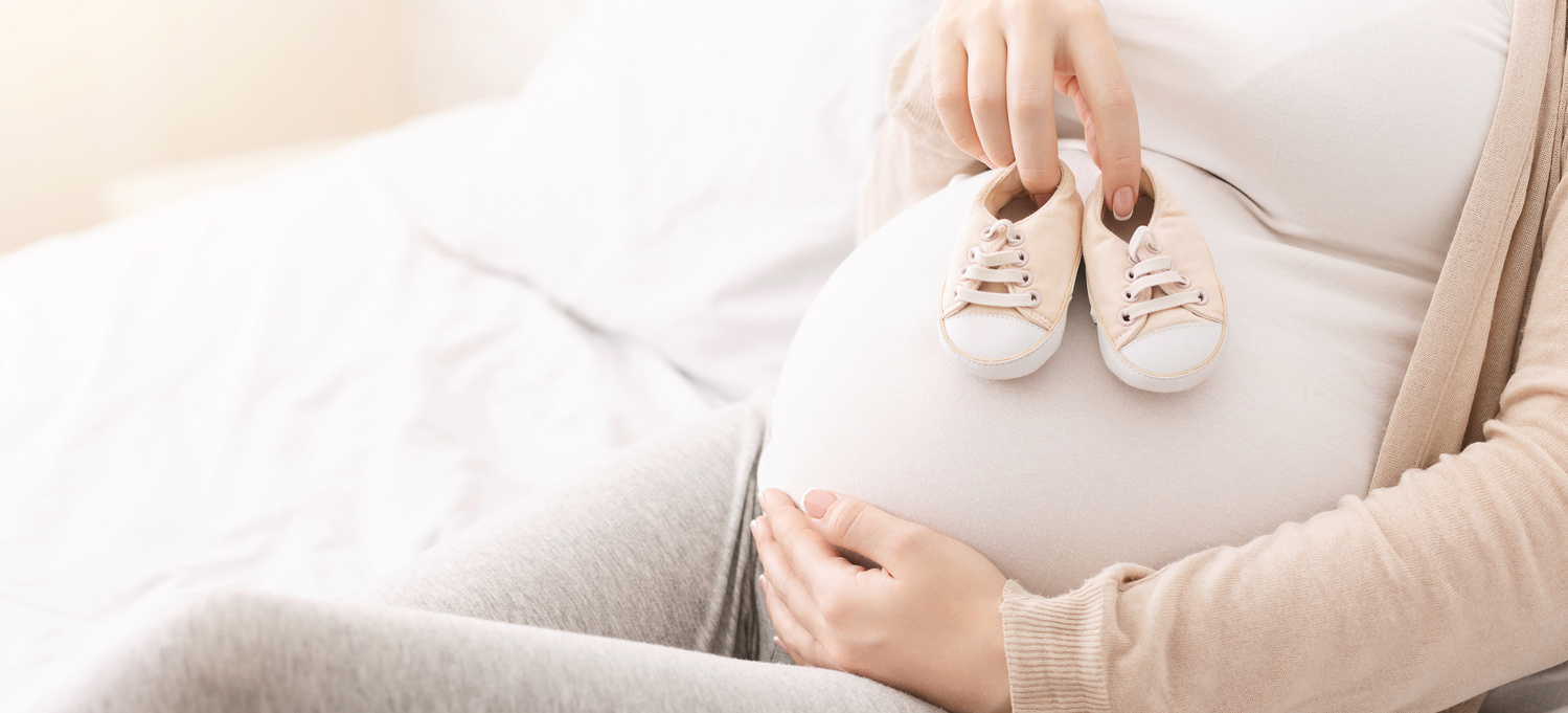 Nėščia moteris ant pilvo laiko kūdikio batukus