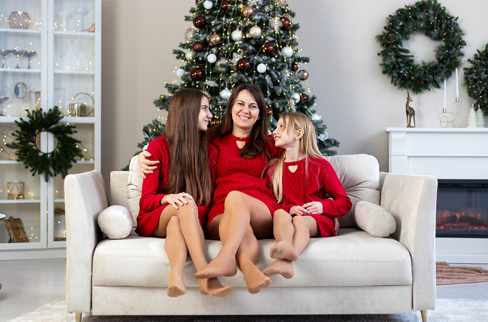 Mama ir jos dukros, vilkinčios raudonas sukneles, kartu leidžia šventinį laiką prie eglutės.