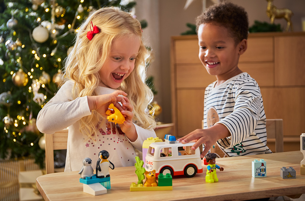 Du vaikai žaidžia su LEGO blokeliais po Kalėdų eglute.