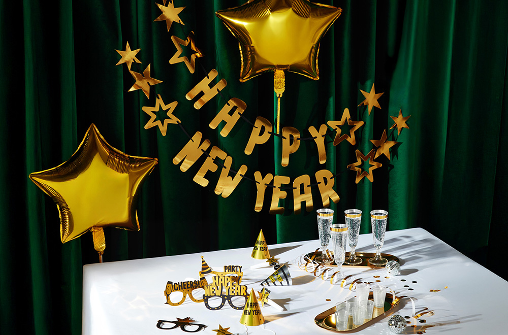 Stalas, dekoruotas Naujųjų metų šventei, su balionais, stiklinėmis ir auksiniais papuošimais.