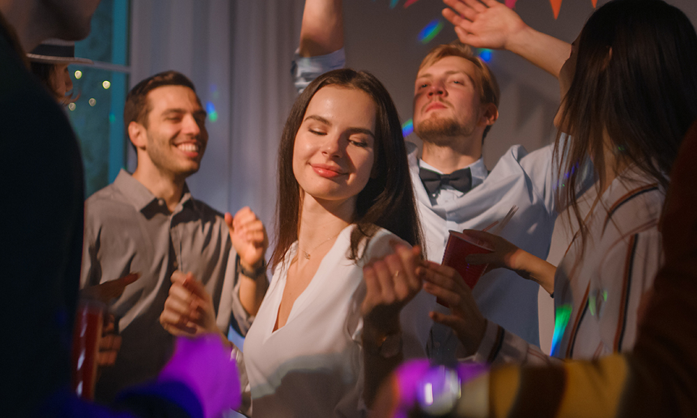 Grupė žmonių šoka vakarėlyje, tarp jų moteris, mėgaujanti muziką.